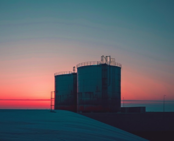 A minimalist photograph capturing the silhouette of two industrial storage tanks against a vibrant sunrise