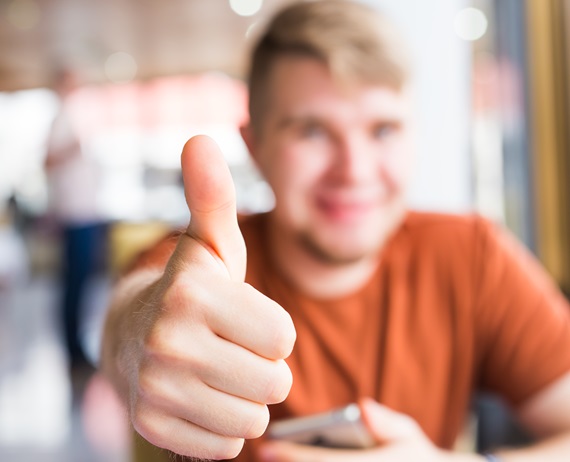 technology, communication and people concept - Young man holding a smart phone with thumbs up