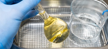 Scientist in blue rubber puts a yellow solution in the flask and beaker for dissolving or extraction into ultrasound bath. Urea analysis. Clinical, toxicological and forensic analysis