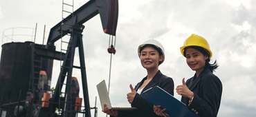 Two female engineers stand beside working oil pumps with a white