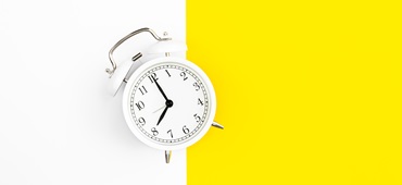 White alarm clock on a white and yellow background, flat lay.